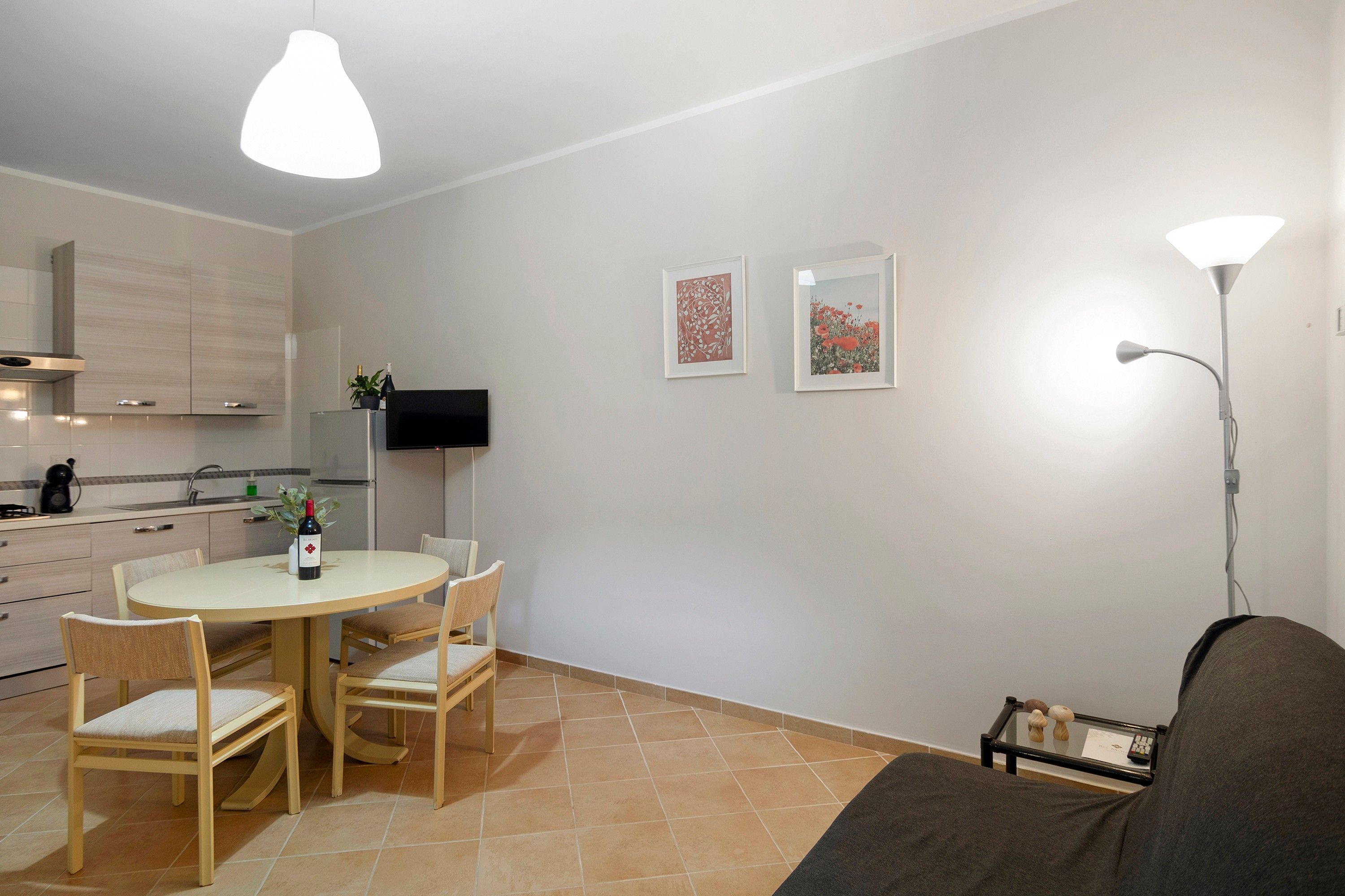 A modern kitchen with a dining area, a flat-screen TV, and two framed artworks on the wall.