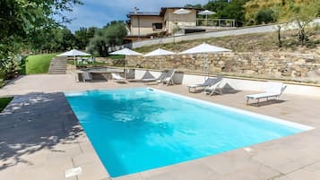 Una piscina rectangular con un muro de piedra y una casa al fondo.