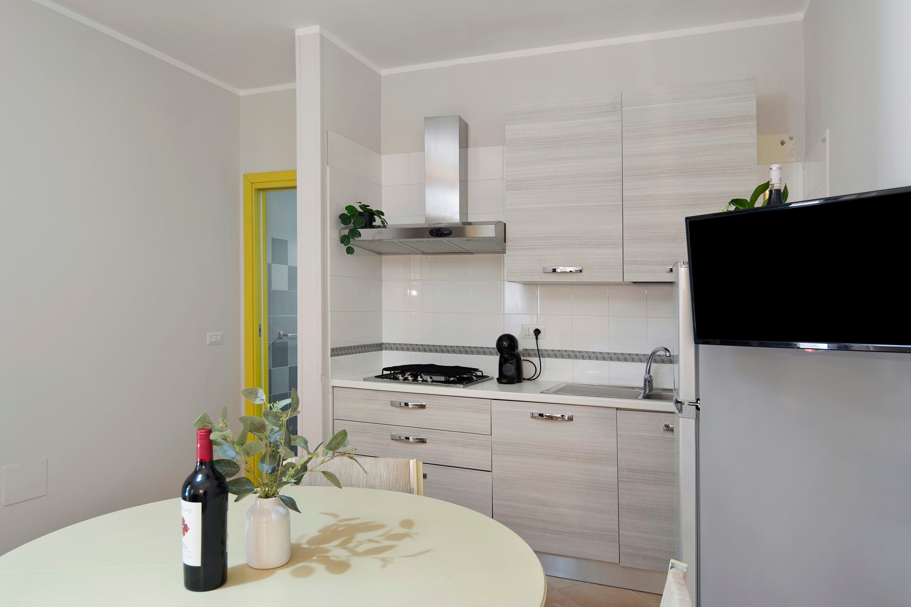Eine moderne Küche mit Gasherd, Kaffeemaschine und integriertem Backofen. Ein Esstisch steht bereit, mit einer Weinflasche und einem Blumenstrauß darauf.