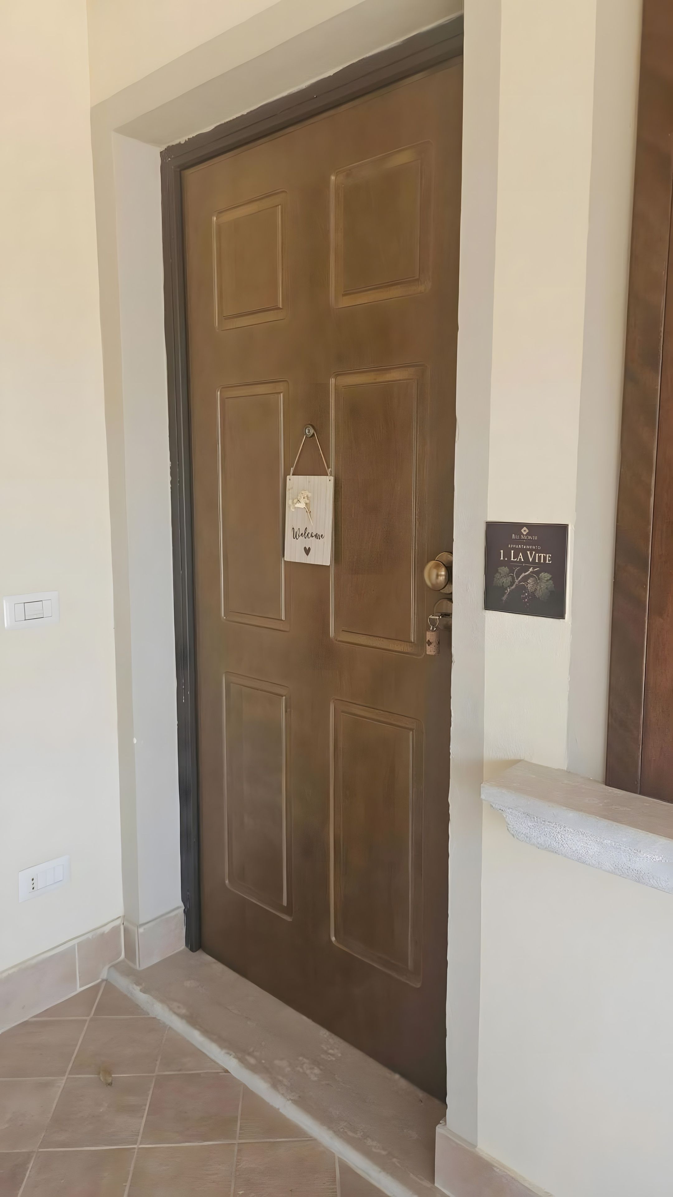 Una puerta marrón con un letrero de bienvenida y una señalización que indica el apartamento '1. La Vite'.