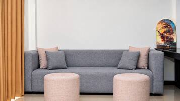 Un sofá gris con dos cojines y dos otomanas redondas en una habitación moderna con una pared lisa y un cuadro enmarcado.