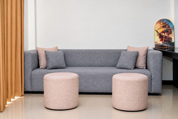 A grey sofa with two cushions and two round ottomans in a modern room with a plain wall and a framed picture.