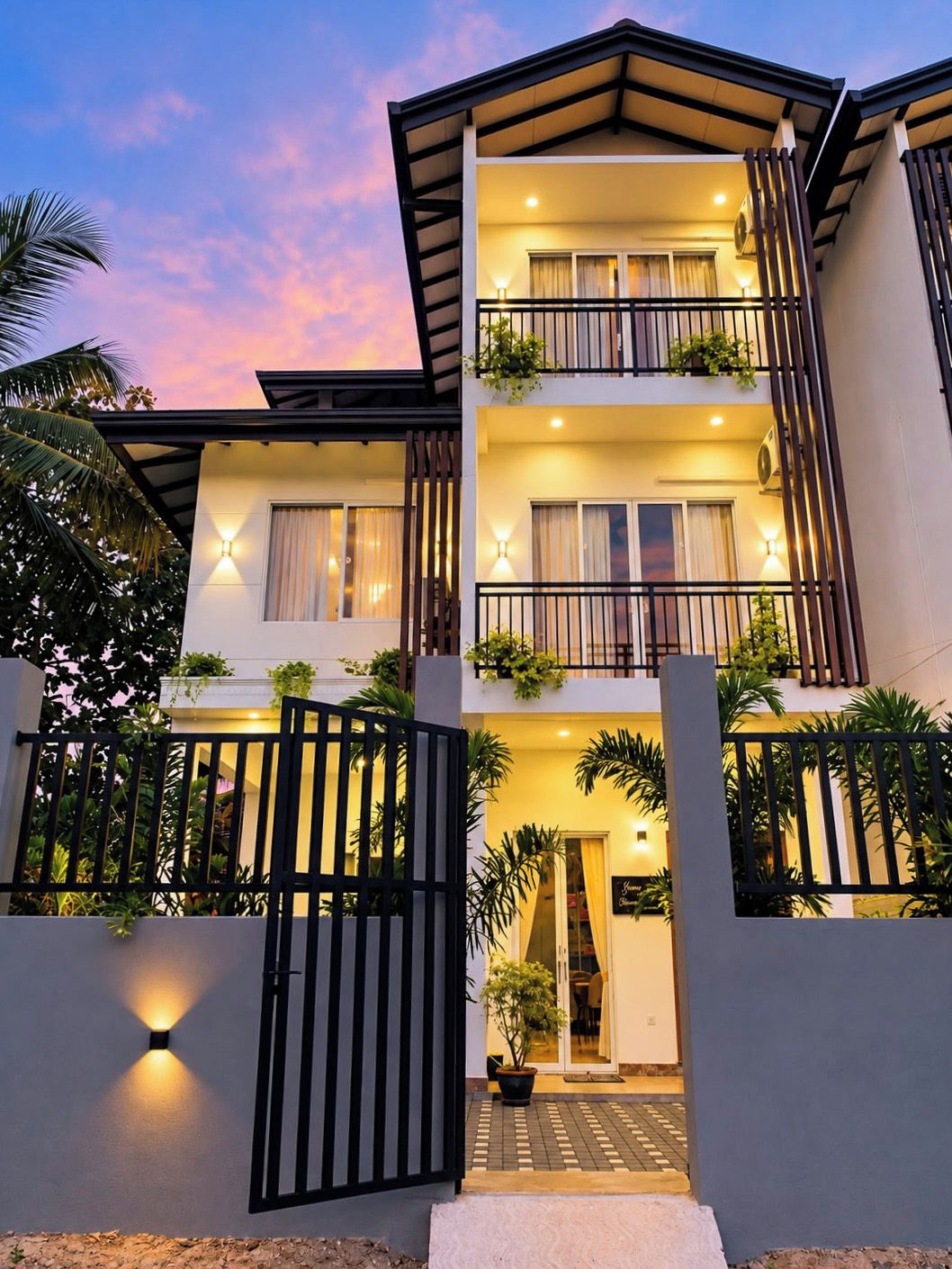 A two-story residential building with a balcony on the upper floor, a gated entrance, and a well-lit facade.
