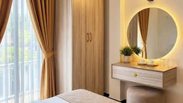 A hotel room with a bed, a wardrobe, a vanity with a mirror, and a window with curtains.