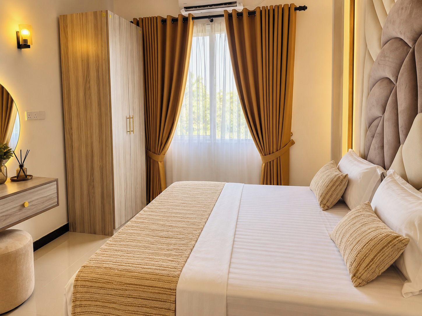 A bedroom with a bed, curtains, a bedside table, and a wall-mounted air conditioning unit.