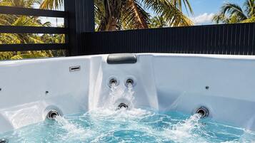 Un jacuzzi con chorros de agua, rodeado por una terraza de madera y palmeras.