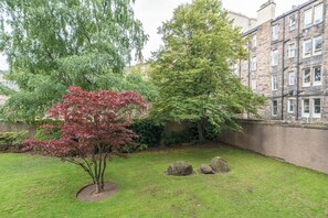 A garden with a tree with red leaves, a large tree, and a stone wall. - Beautiful 1-Bed on Brunswick | Edinburgh East End - Pass the Keys (Edinburgh)