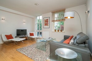 A modern living room with a flat-screen TV, a glass coffee table, and a grey sofa with orange cushions. - Beautiful 1-Bed on Brunswick | Edinburgh East End - Pass the Keys (Edinburgh)