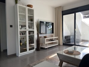 Ein modernes Wohnzimmer mit einer Glasschrank, einem Flachbildfernseher und einer Schiebetür zu einem Außenbereich.