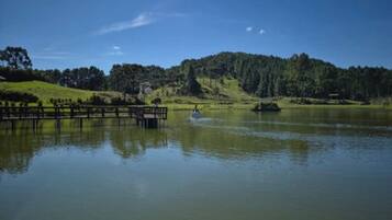 Un lago tranquilo con un muelle de madera que se adentra en el agua, rodeado de colinas verdes y árboles bajo un cielo despejado.