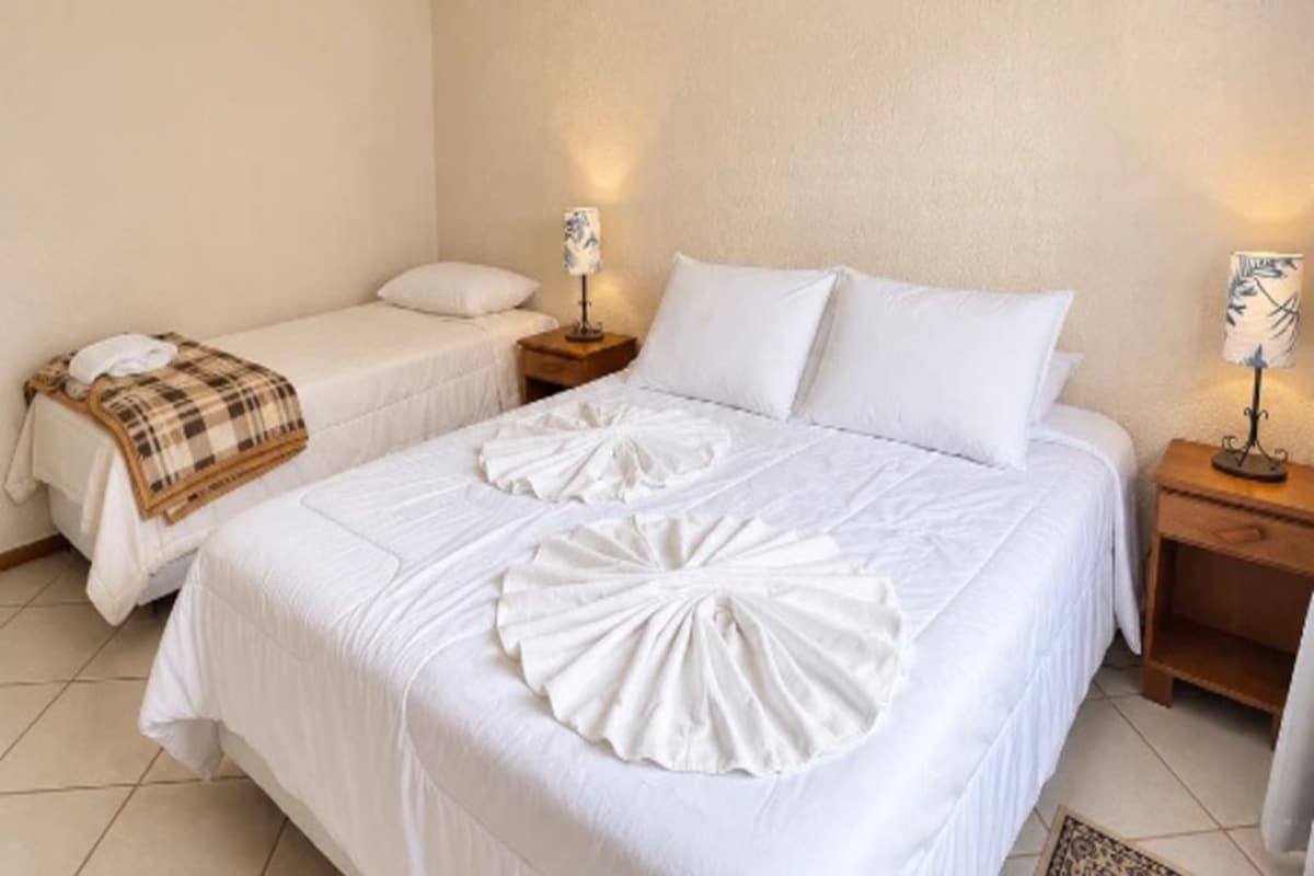 Habitación de hotel con una cama grande, una cama más pequeña, dos mesitas de noche y una lámpara sobre cada una.