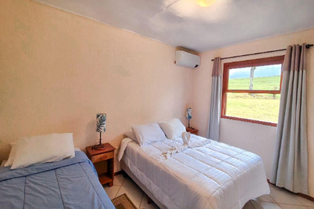 Un dormitorio con dos camas, una ventana con cortinas, una mesita de noche con lámpara y un aire acondicionado de pared.