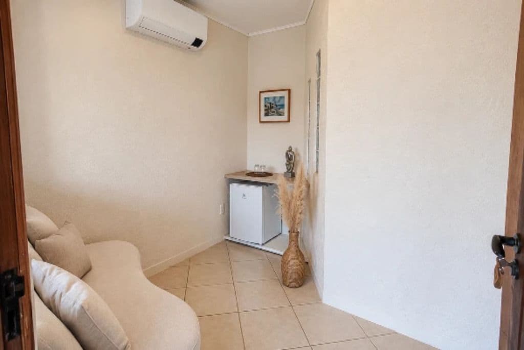 A room with a beige sofa, a small white cabinet, a decorative vase, and a door.