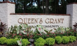 Schild für 'Queen's Grant' mit einer Ziegelwand und einem Garten mit verschiedenen Pflanzen.