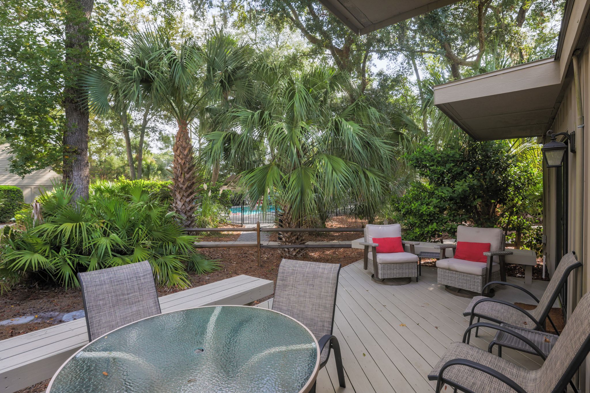 An outdoor patio with a round table and chairs, surrounded by lush greenery and trees.