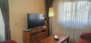 Una habitación con una televisión de pantalla plana sobre un soporte de madera, una lámpara, un control remoto y una pequeña mesa con un adorno.
