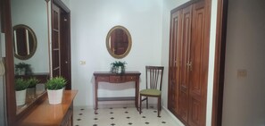 Un pasillo con un aparador de madera, una mesita con planta en maceta, una silla y un espejo en la pared.