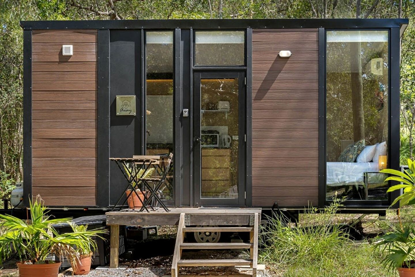 A modern cabin with a sliding door entrance, a small outdoor seating area, and a visible bed inside.