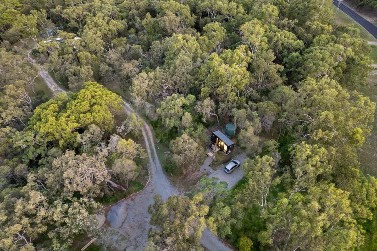 Una cabaña aislada rodeada de un bosque denso, accesible por un camino estrecho.