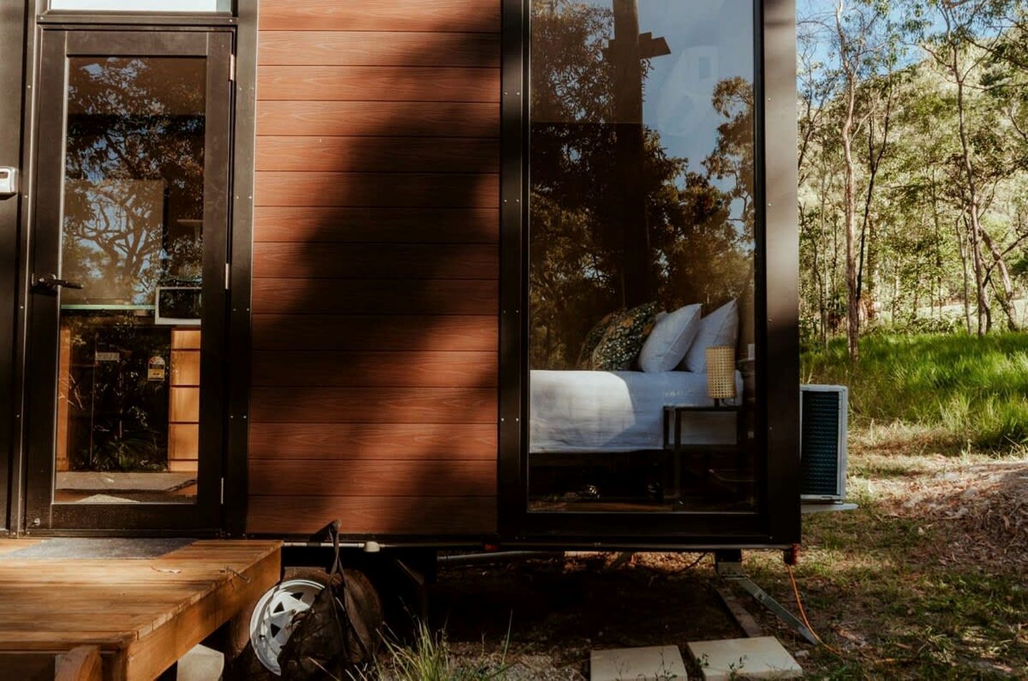 A small, modern cabin with a sliding glass door leading to a bedroom with a bed and a nightstand.