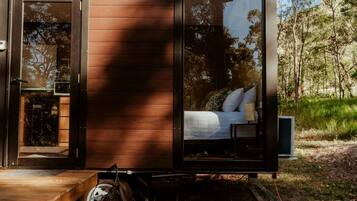 A small, modern cabin with a sliding glass door leading to a bedroom with a bed and a nightstand.