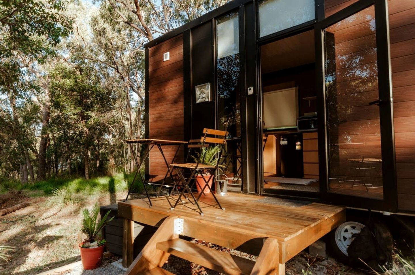 A modern wooden cabin with a deck, outdoor seating, and a visible kitchen area.
