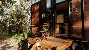 A modern wooden cabin with a deck, outdoor seating, and a visible kitchen area.