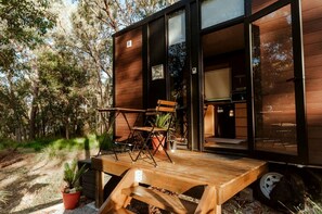 A modern wooden cabin with a deck, outdoor seating, and a visible kitchen area.
