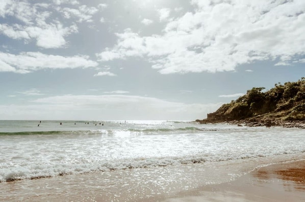 A beach with waves, a clear sky, and a rocky outcrop.