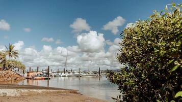 A marina with boats docked, a sandy shore, and a clear sky with clouds.