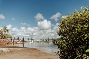 A marina with boats docked, a sandy shore, and a clear sky with clouds.
