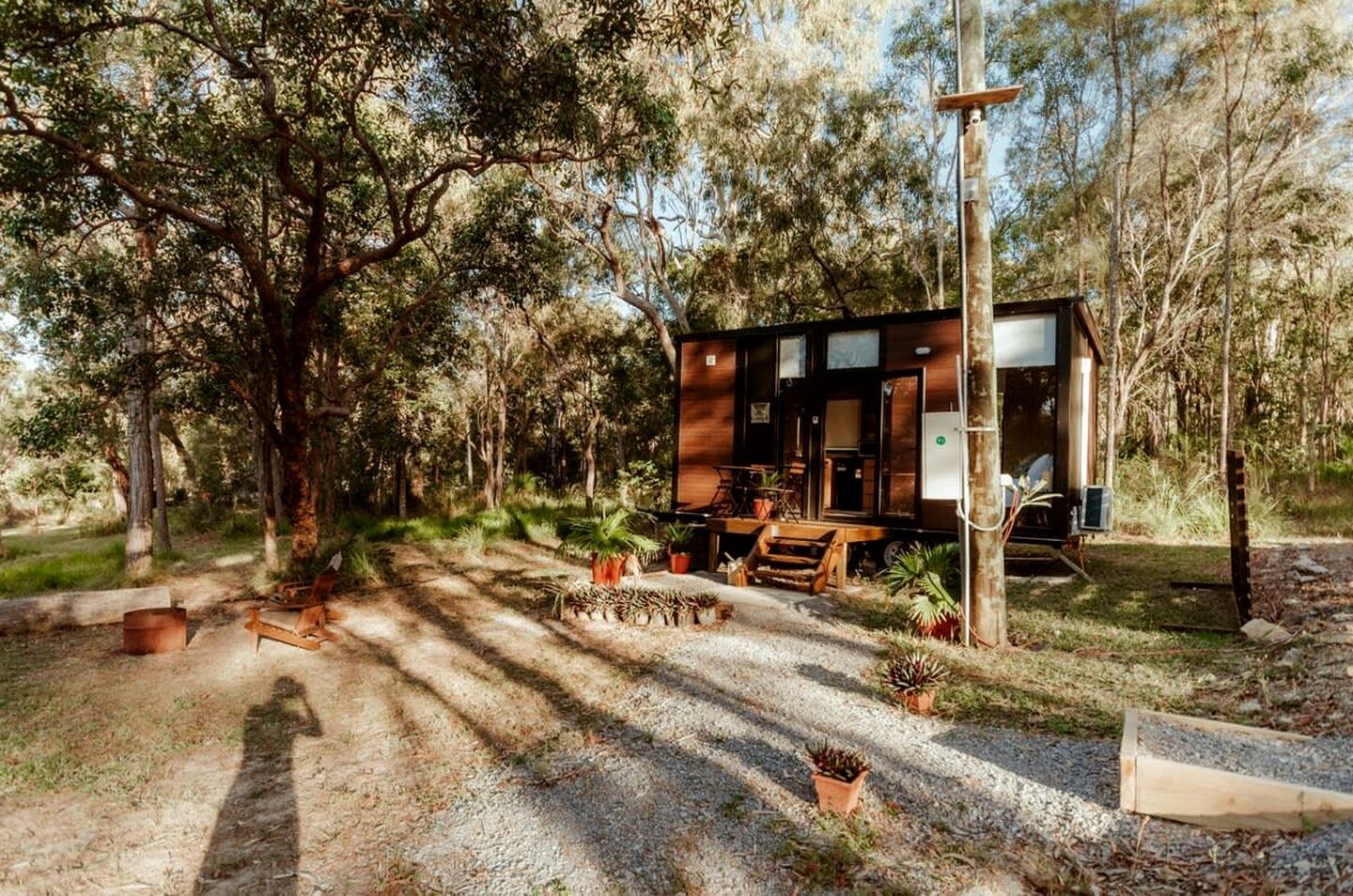 A cabin with a gravel driveway, surrounded by trees, and equipped with outdoor furniture.