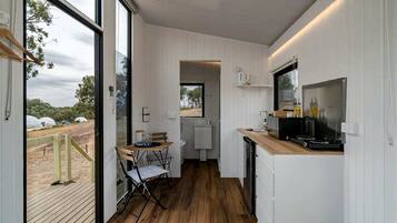 A compact kitchen with a wooden floor, a dining area with a table and chairs, and a large window offering a view of the outdoors.