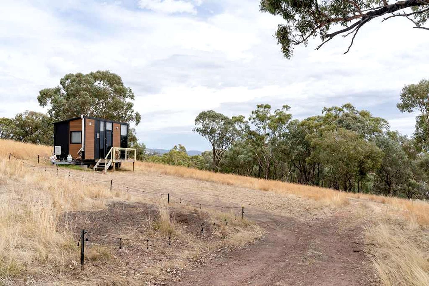 A single-story cabin with a wooden exterior and a small porch, surrounded by dry grass and trees.