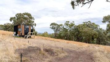 A single-story cabin with a wooden exterior and a small porch, surrounded by dry grass and trees.
