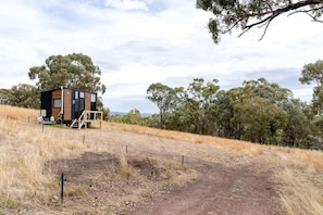 A single-story cabin with a wooden exterior and a small porch, surrounded by dry grass and trees.