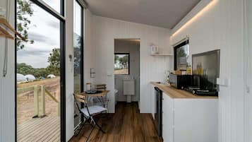 A compact kitchen with a wooden floor, a dining area with a table and chairs, and a large window offering a view of the outdoors.