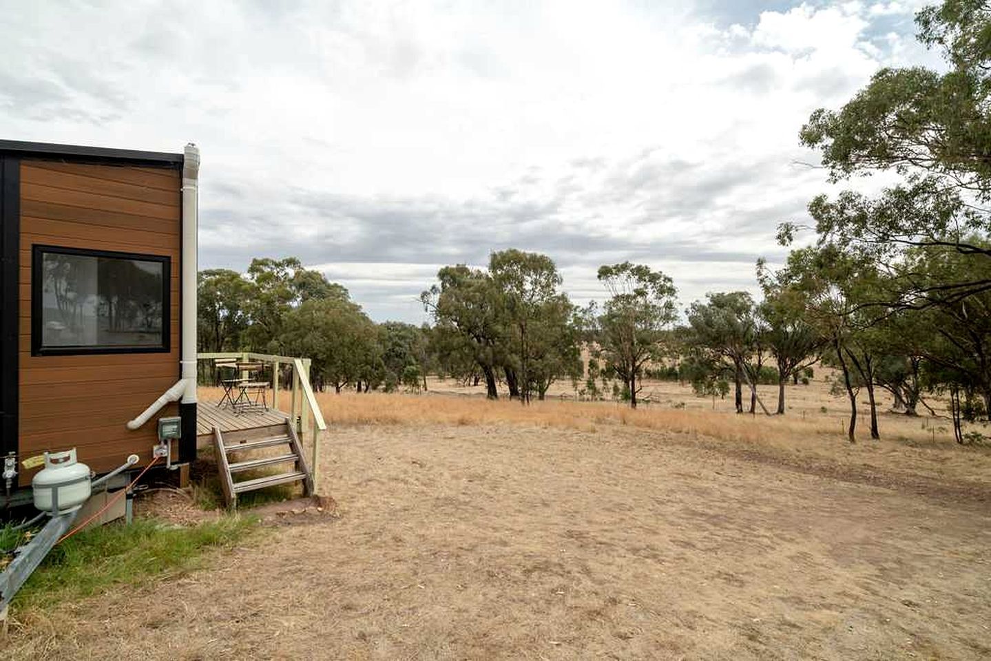 A mobile home with a deck and outdoor area, surrounded by trees and dry grass.