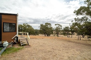 A mobile home with a deck and outdoor area, surrounded by trees and dry grass.