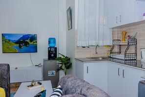 A compact living space with a sofa, a coffee table, a TV, a water dispenser, a kitchen area with cabinets and a sink, and a plant. - An good place to be,with Mt Kenya view,a quiet place ,with a spacious parking (Nanyuki)