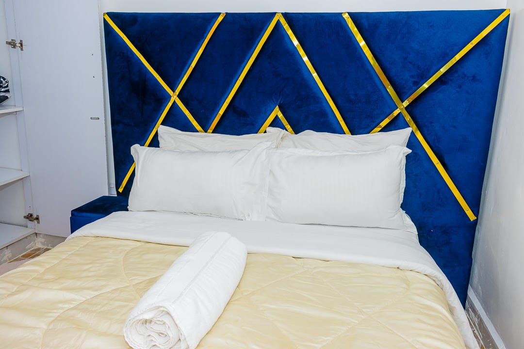 A bed with a blue headboard, white bedding, and a rolled towel.
