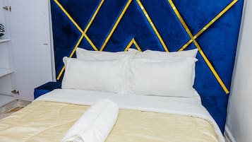 A bed with a blue headboard, white bedding, and a rolled towel.