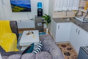 A living room with a sofa, a coffee table, and a TV. There is a kitchen area with a sink and cabinets. - An good place to be,with Mt Kenya view,a quiet place ,with a spacious parking (Nanyuki)