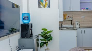 A compact living space with a flat-screen TV, a water dispenser, a small plant, and a kitchenette area.