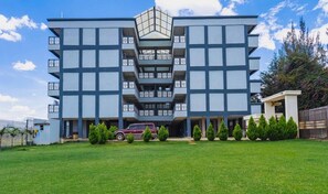 A multi-story building with a central atrium, a car parked in front, and a well-maintained lawn. - An good place to be,with Mt Kenya view,a quiet place ,with a spacious parking (Nanyuki)