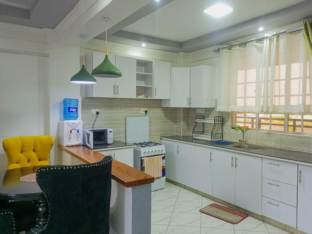 A modern kitchen with white cabinets, a stove, microwave, and a dining area with a yellow chair.
