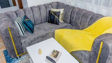 A grey sofa with yellow accents, a white coffee table, and a blue patterned rug.
