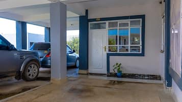 A parking garage with two cars parked, a white door with a window, and a potted plant.