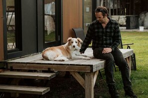 Una persona sentada en un banco de madera al aire libre con un perro a su lado.