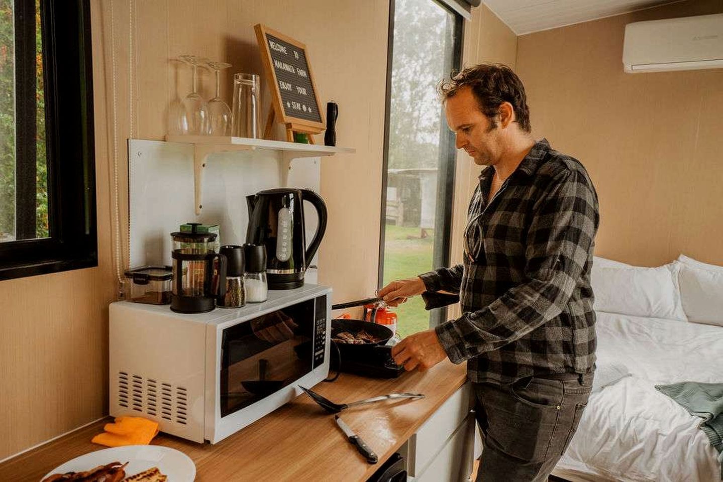 A person cooking in a kitchenette with a microwave, coffee maker, and various kitchen utensils.